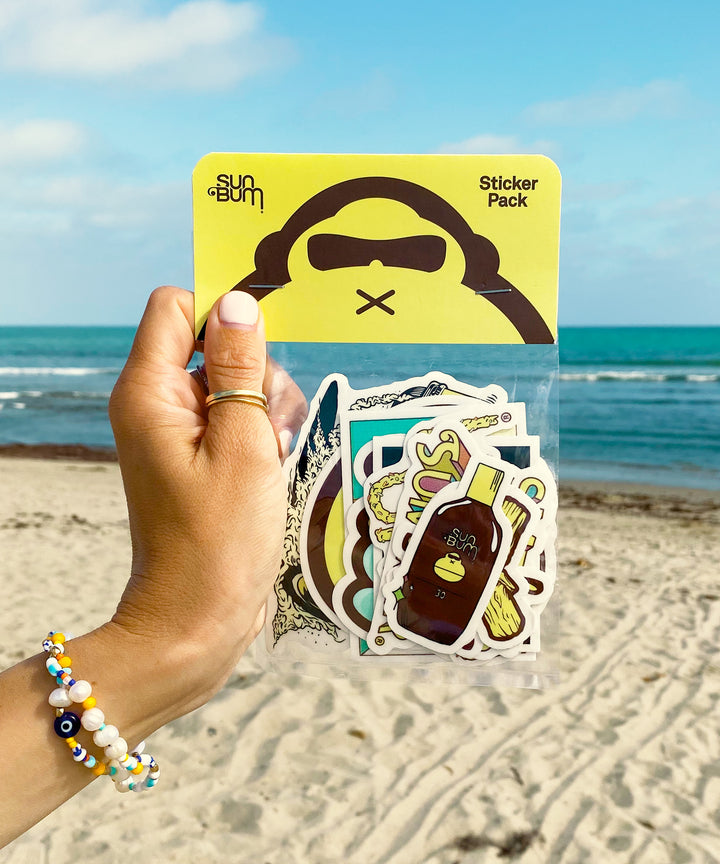 Hand holding a pack of 10 vinyl stickers with vibrant designs, perfect for decorating your surf gear. Only available here and at your local surf shop. Sun Bum.