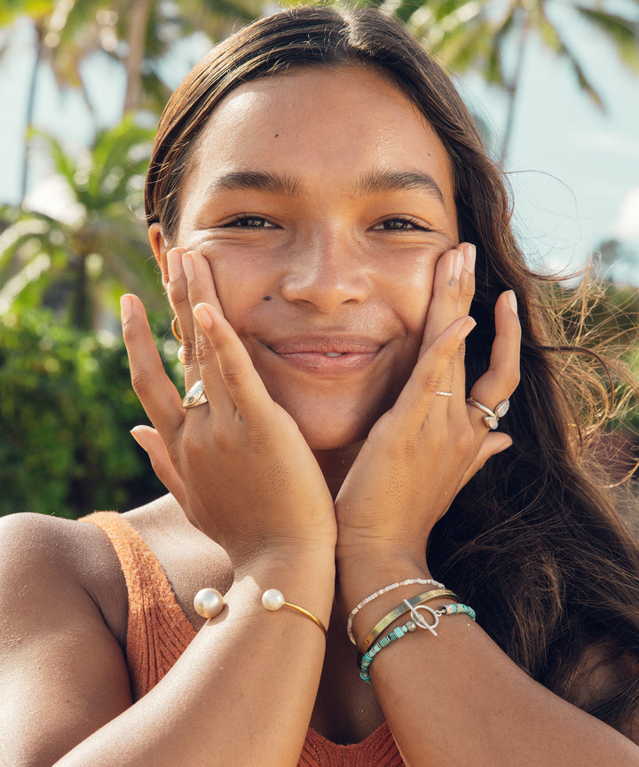 Woman smiling and gently holding her face, showcasing glowing skin after using Sun Bum's Daily 50 Face Lotion enriched with Vitamin E and Antioxidants for 24-hour moisture and UVA/UVB protection.