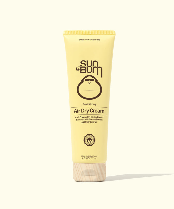 Yellow tube of Air Dry Cream & Hair Towel Kit featuring Sun Bum's signature monkey logo, positioned against a light background. The revitalizing hair styling product promises enhanced natural style - by Sun Bum