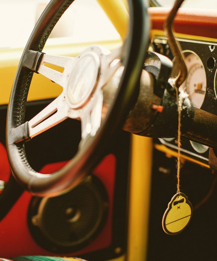 Retro car steering wheel and dashboard, capturing the essence of the Original Scent Air Freshener that helps eliminate car odors like decaying burritos, wet bikinis, and petrified french fries. Sun Bum