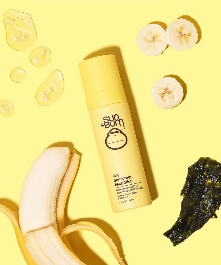 Daily Sunscreen Face Mist SPF 30 by Sun Bum, surrounded by banana slices, banana peel, and brown algae on a bright yellow background.