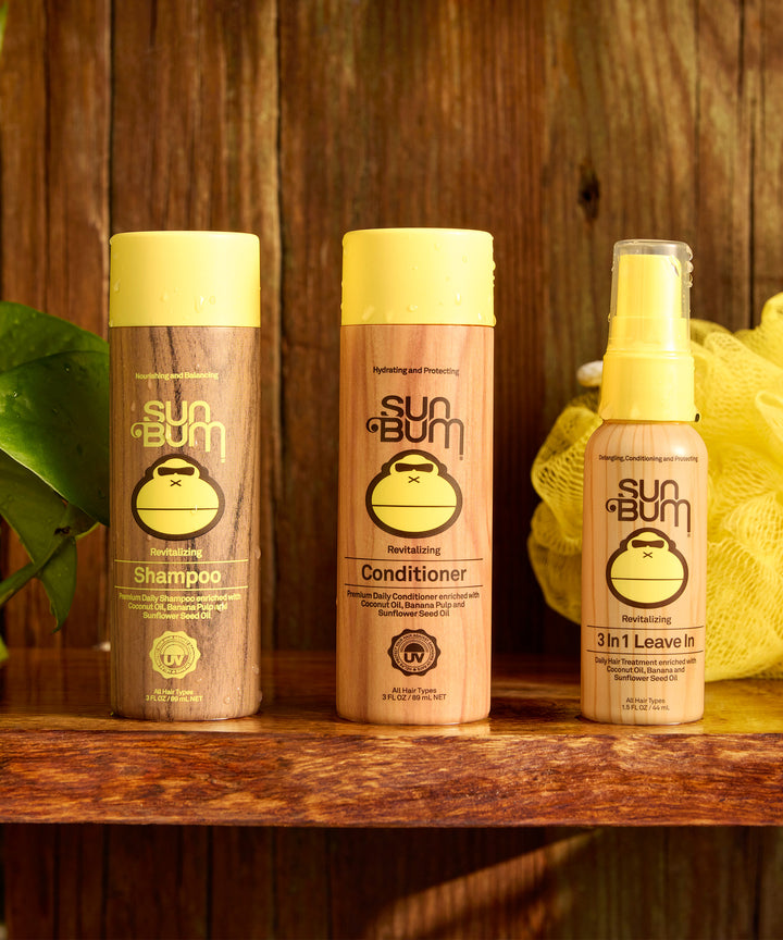 Revitalizing Conditioner bottle with banana-based formula displayed on wooden shelf alongside complementary hair care products from Sun Bum, featuring signature monkey logo and yellow cap design - by Sun Bum