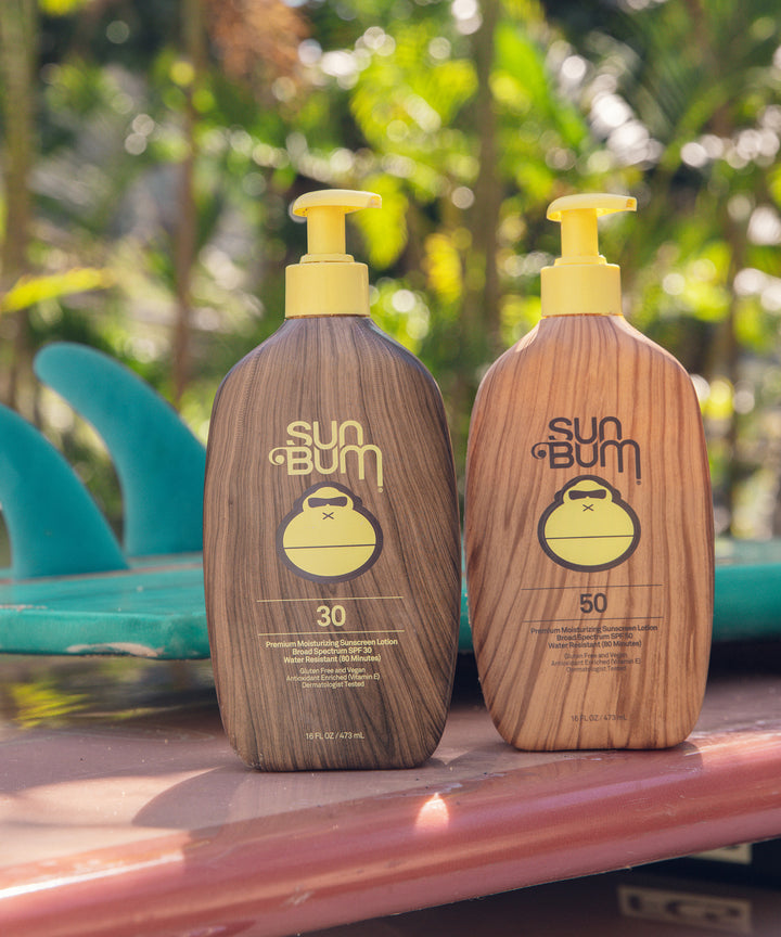 Original SPF 30 Sunscreen Lotion on display outdoors with classic Sun Bum packaging and surfboards in the background, Sun Bum