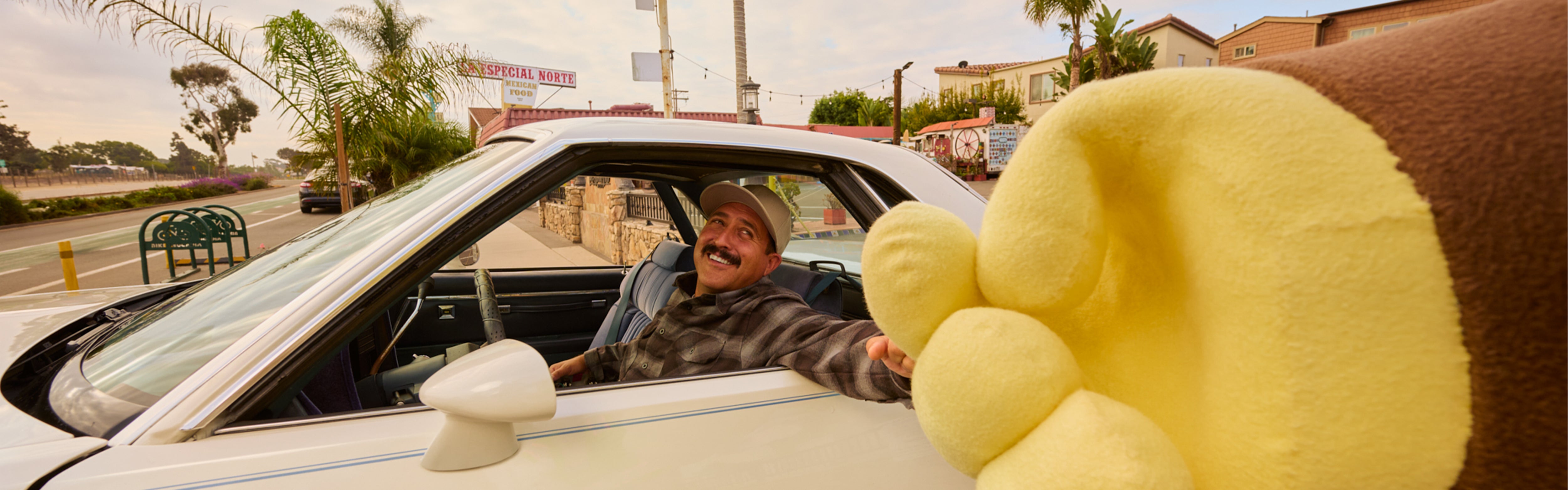 Man smiling from a car window giving a high five to a giant Sonny hand, featuring the SB Shop All Collection – Sun Bum.