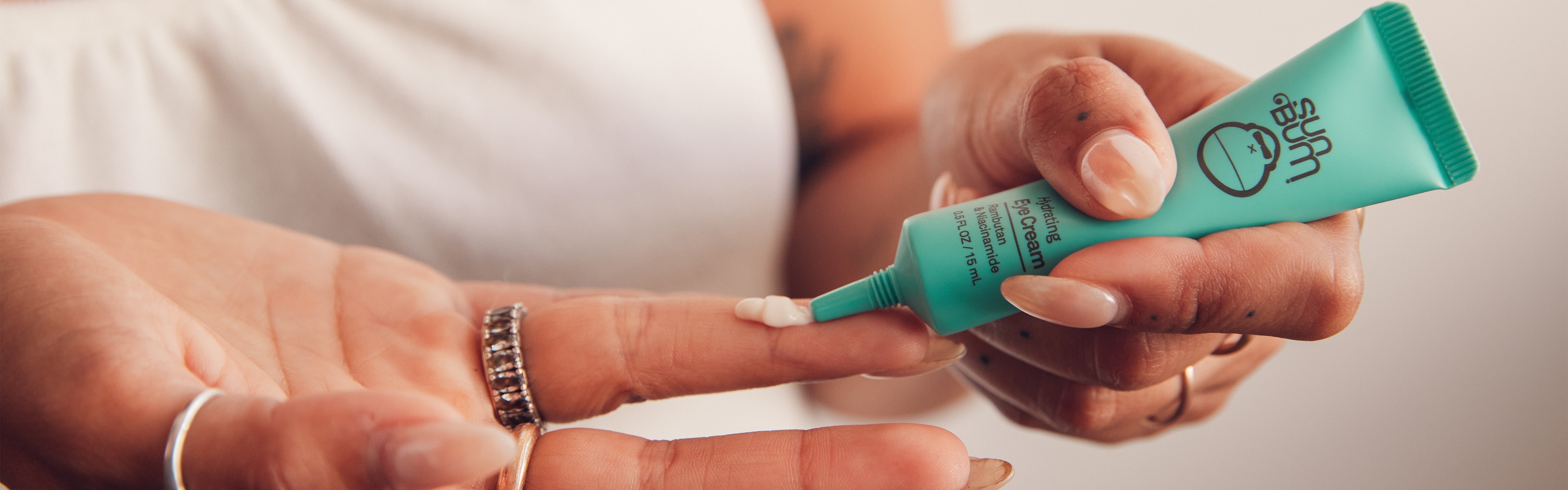 Close-up of hands applying eye cream from a turquoise tube, highlighting the SB Hydrating Skin Care Collection – Sun Bum.